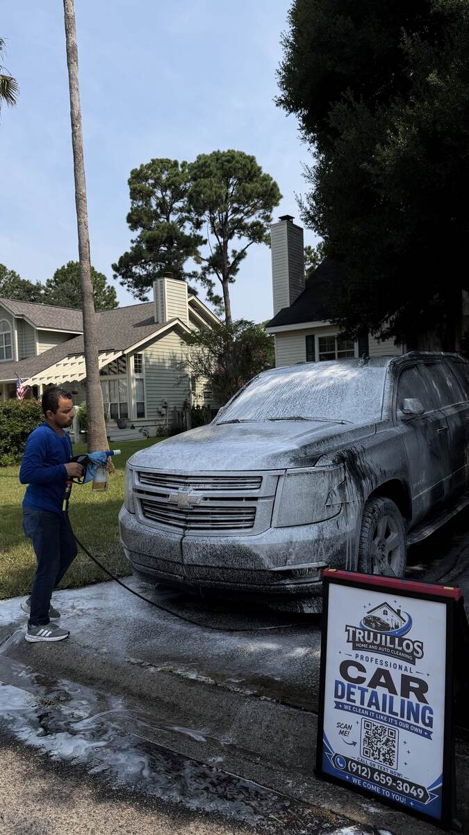 Trujillo's Cleaning Services team member foam-washing an SUV in a driveway
